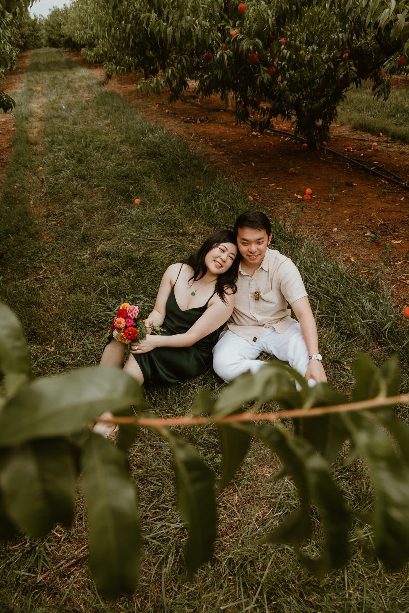 Jeffrey and Katie sitting in the grass of a peach orchard